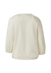 Blusa leggera color crema, maniche lunghe a sbuffo, tessuto strutturato, scollatura tonda e orlo curvato. Nessun bottone o decorazione visibile.