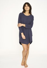 Vestido azul marino de manga larga en tejido suave, con escote redondeado, bolsillos laterales y una parte trasera ligeramente más larga. Diseño minimalista.