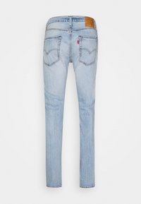 Jean en denim bleu clair avec jambes droites, deux poches arrière, une petite étiquette rouge sur la poche droite et un patch de marque en cuir marron sur la ceinture.