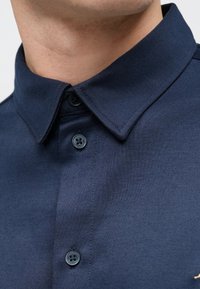 Marineblauw poloshirt met een gestructureerde stof, voorzien van een standaardkraag en twee donkere knopen aan de knoopsluiting.