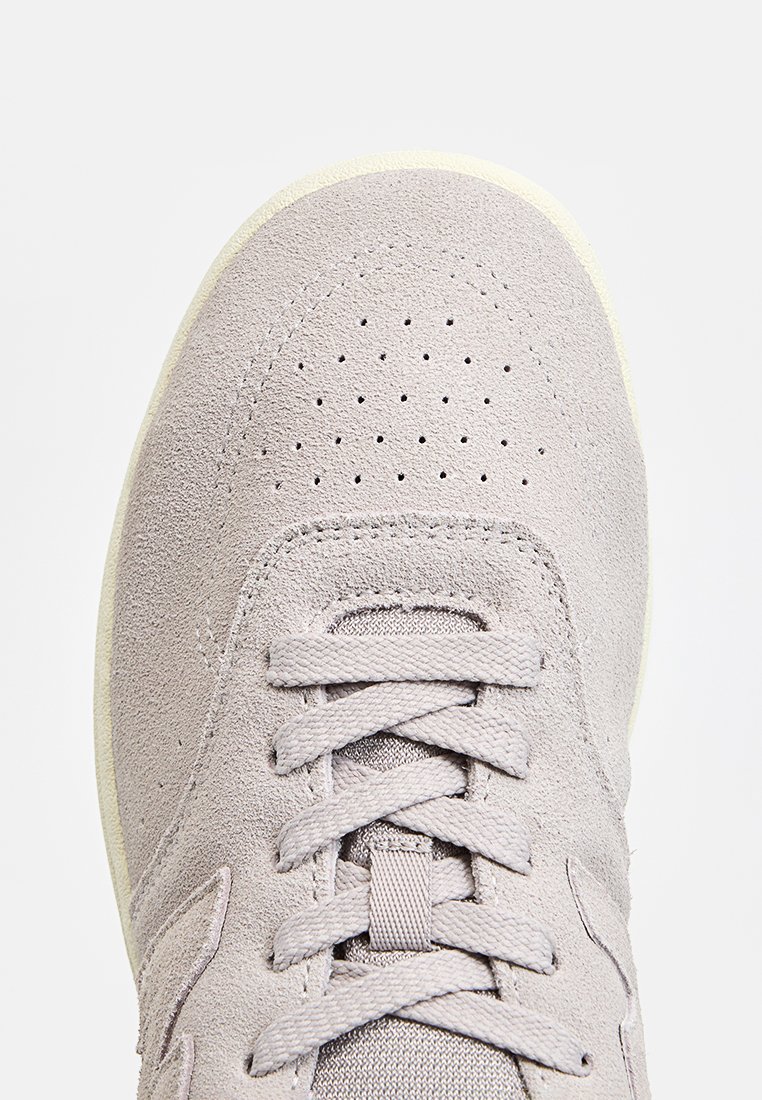 Zapatilla de ante gris claro, con puntera perforada, cordones planos y una suave suela de goma con sutiles acentos texturizados.