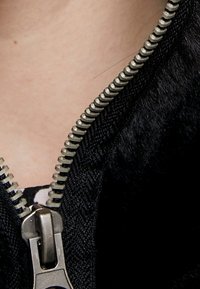 Czarna tkanina z zamkiem błyskawicznym wykonanym z metalowego srebra. Tkanina wydaje się mieć fakturę i miękkie wykończenie. Zamek jest cz�ęściowo otwarty, odsłaniając wewnętrzną warstwę.