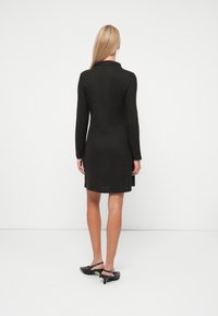 Μαύρο φόρεμα με μακριά μανίκια από ριμπ ύφασμα, μέχρι το γόνατο, με στρογγυλή γιακά και χαλαρή εφαρμογή, συνδυασμένο με μαύρα slingback τακούνια.