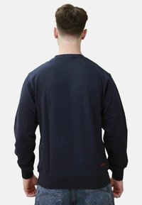 Felpa navy con maniche lunghe, polsini e orlo a costine, texture morbida e piccolo logo arancione dettagliato in basso a sinistra.