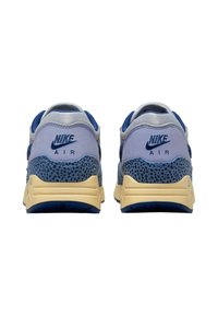 Nike Air sneakers med en ljusblå ovandel, mörkblå detaljer, texturerad grå baksida och en krämfärgad sula med ett mönstrat overlay.