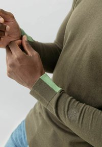 Olijfgroen sweater met geribbelde mouwen in lichtgroen. Heeft een subtiele logostijl op de mouw. Soepele textuur en aansluitend ontwerp.