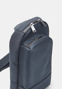 Borsa compatta blu navy con una parte frontale in pelle texturizzata e una parte posteriore in tessuto liscio. Presenta due scomparti con zip e una tracolla regolabile.