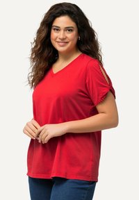 Camiseta roja de cuello en V hecha de algodón; cuenta con mangas cortas con detalles de pompones en los puños y un corte relajado.