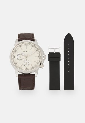 Montre chronographe argentée avec cadran crème et bracelet en cuir texturé marron, accompagnée d'un bracelet de remplacement en silicone noir.