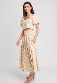 Dwuczęściowy zestaw składający się z krótkiego topu na ramiączkach z kwadratowym dekoltem oraz długiej, zwiewnej spódnicy. Wykonany z materiału w kratę w odcieniach beżowym i białym.