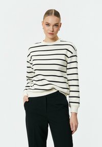 Svart- och vitrandig sweatshirt i mjukt tyg, med rund halsringning och ribbade ärmslut, tillsammans med svarta byxor.