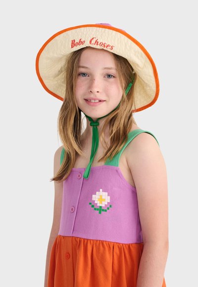 Jeune fille portant un chapeau crème à large bord avec une bordure orange et une robe sans manches violette et orange avec un petit motif floral.