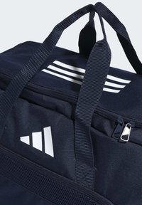 Donkerblauwe sporttas gemaakt van duurzaam materiaal, met witte gestreepte accenten en logo. Dubbele handvatten voor gemakkelijke draagbaarheid, met ritssluiting.
