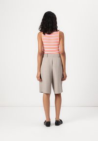 Stripet løs tanktopp i rosa og hvit, kombinert med beige skræddershorts med belte i midjen og løs passform. Sorte flate sko fullfører looken.