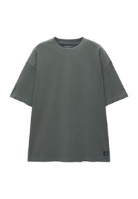 T-shirt grigia oversize in cotone con colletto a coste, maniche corte e un piccolo logo sulla parte inferiore sinistra. Tessuto morbido e vestibilità rilassata.