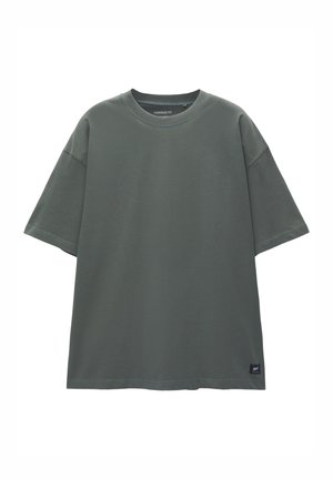 T-shirt grigia oversize in cotone con colletto a coste, maniche corte e un piccolo logo sulla parte inferiore sinistra. Tessuto morbido e vestibilità rilassata.