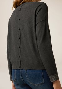 Grå stickad tröja med rundad halsringning, knappar bak och utsmyckade ärmslut med ett strassmönster. Styla med blåjeans.