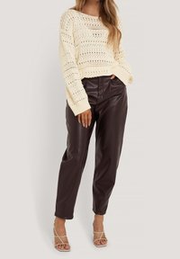 Norsunluunvärinen neulepaita avointa kuviota, yhdistetty korkeavyötäröisiin ruskeisiin keinonahkahousuihin. Rusetilliset, läpinäkyvät korkokengät viimeistelevät asun.