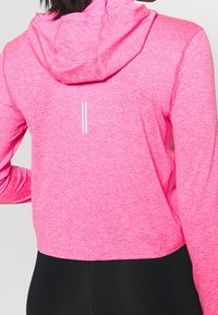 Roze cropped hoodie van een gestructureerde stof, met een kap en witte accenten langs de achterkant. Het ontwerp is eenvoudig met een sportieve uitstraling.