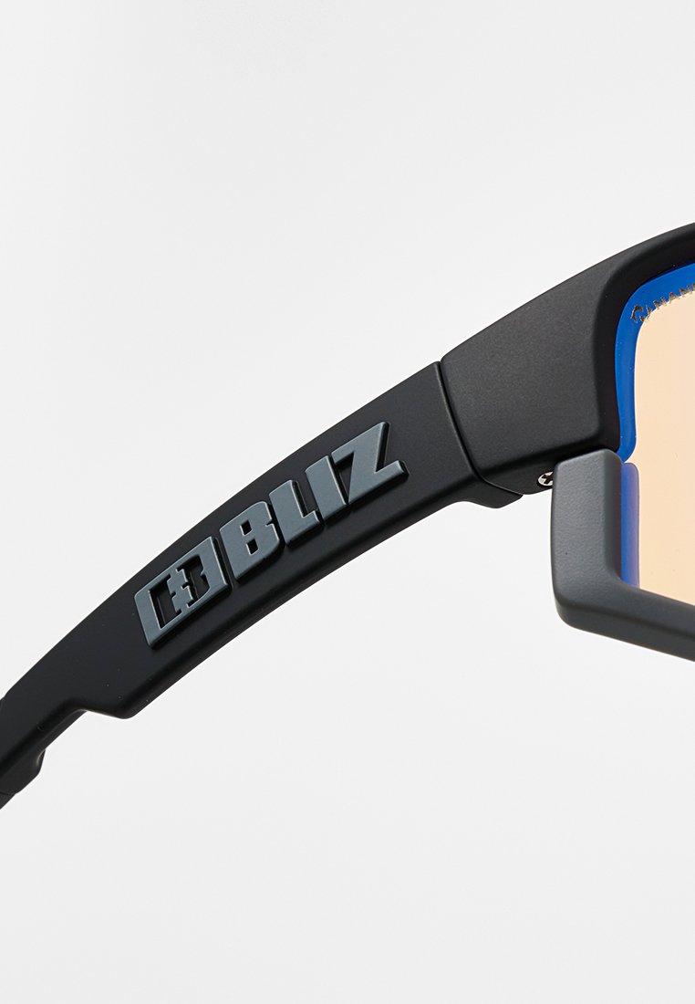 Schwarzer Sonnenbrillenarm mit erhabenem grauen "BLIZ"-Logo und einem Teil des beigen Glases mit sichtbarem blauen Innengestell.