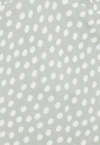 Tissu gris clair avec une texture douce, présentant des pois ovales blancs irréguliers répartis uniformément sur la surface.