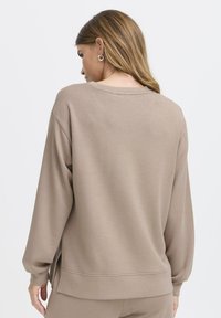 Sweat-shirt marron à manches longues avec une coupe décontractée, des poignets côtelés et des fentes latérales. Texture lisse, design minimaliste et col rond.