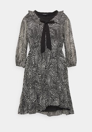 Robe noire longueur genou avec motif à pois blancs dispersés, manches trois-quarts transparentes, col volanté et nœud noir au niveau du col.