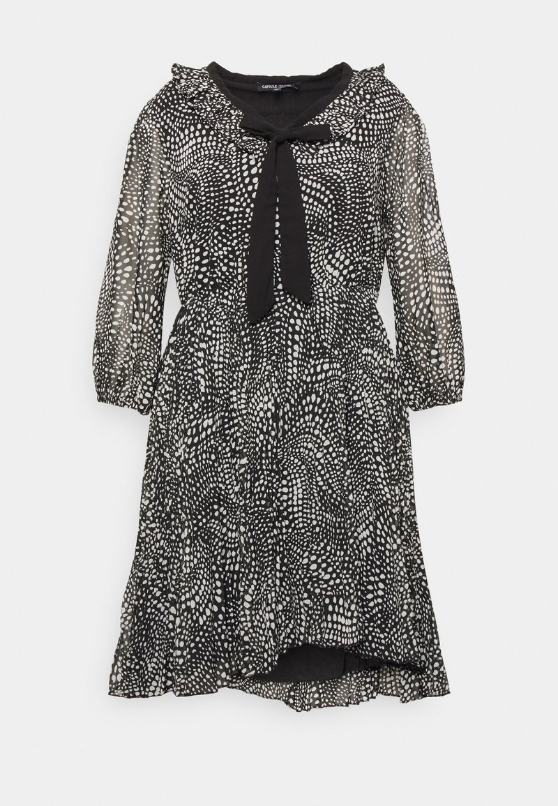 Robe noire longueur genou avec motif à pois blancs dispersés, manches trois-quarts transparentes, col volanté et nœud noir au niveau du col.
