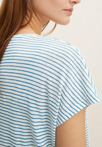 Pruhované tričko v bílém a modrém, krátké rukávy, s uvolněným střihem a měkkou, texturovanou tkaninou s horizontálními pruhy.