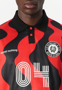 Red and black polo shirt with wavy patterns, collar, and button front. Features "admit nothing" text and a circular logo on the chest.