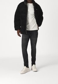 Svart fleecejacka med dragkedja, vit t-shirt under, mörka jeans och ljusa sneakers. Enkel design, avslappnad passform.