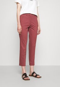Roze gekleurde broeken met een getailleerde pasvorm, rechte pijpen en subtiele plooien. Gecombineerd met zwarte platte sandalen met een brede band.