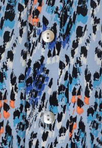 Tessuto azzurro chiaro con stampe astratte di colore nero, bianco, blu e arancione, caratterizzato da due bottoni rotondi lucidi argentati cuciti verticalmente.