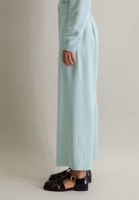 Vaaleansiniset leveälahkeiset housut, joissa on sileä pinta ja elastinen vyötärö, yhdistettynä mustiin sandaaleihin, joissa on solki ja leikattu muotoilu.