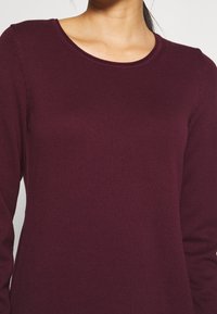 Burgundy långärmad topp med ribbat mönster, rund halsringning och åtsittande design, tillverkad av mjukt, elastiskt tyg.