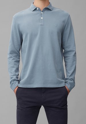 Polo de manga larga en algodón azul claro, con cuello clásico, tapeta de tres botones y logo bordado sutil en el pecho.