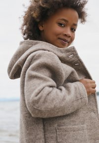 Beige wollen coat met een capuchon, voorzien van een gestructureerde stof, zijzakken en een open voorkant met met stof bedekte knopen.