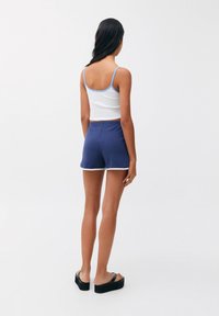 Débardeur blanc à côtes avec des bretelles bleu clair, associé à un short bleu foncé bordé de blanc. Sandales plates à plateforme noires.