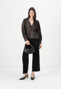 Bluzica s leopard uzorkom i dugim rukavima, u paru s crnim širokim hlačama visokog struka i malom crnom torbicom. Crne špic cipele.