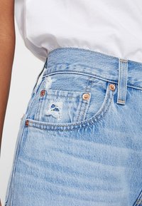 Jean en denim bleu clair à taille haute, avec des accents effilochés, des accessoires de couleur cuivrée et un design classique à cinq poches.