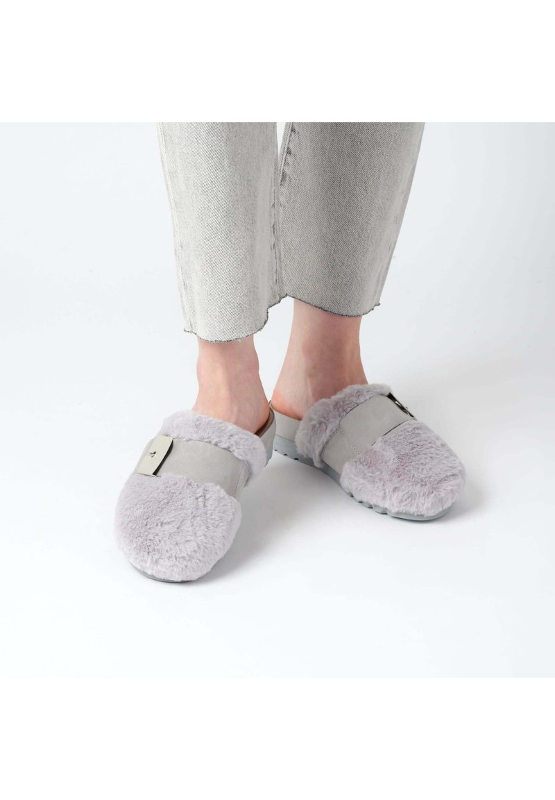 Szare klapki wsuwane z puszystym jasnofioletowym futerkiem na krawędzi, z szerokim paskiem i metalowym akcentem. Miękka faktura i zaokrąglony kształt palców.