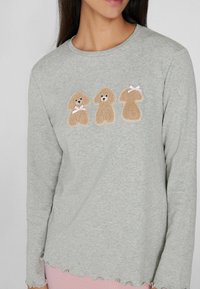Camiseta de manga larga gris con tres diseños de poodles bordados con lazos rosas. Dobladillo festoneado y tela suave y texturizada.