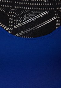 Blå tajt linne med en slät textur nertill, med en svart geometrisk spetsdesign upptill för kontrast och detalj.