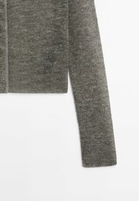 Harmaa neulottu neuletakin hiha, jossa näkyvät napit vasemmalla puolella, esillä valkoista taustaa vasten.