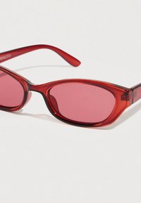 Lunettes de soleil rouges à forme élégante en œil de chat. Fabriquées en plastique lisse, avec des verres teintés roses et des branches rouges fines.