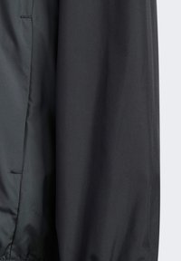 Chaqueta de nylon negra con una textura suave, que cuenta con una cinturilla elástica y mangas ligeramente fruncidas. Diseño minimalista sin logos visibles.