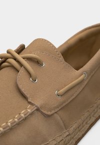 Κοντινό πλάνο ταμπά μοκασίνι από σουέντ με δερμάτινα κορδόνια περασμένα μέσα από μεταλλικά σπιράλ και λεπτομερείς ραφές κατά μήκος της άκρης της σόλας.