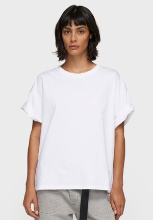 Witte oversized t-shirt met korte, opgerolde mouwen en een ronde halslijn. Bevat subtiele borduursels op de borst. Zacht katoenen stof.