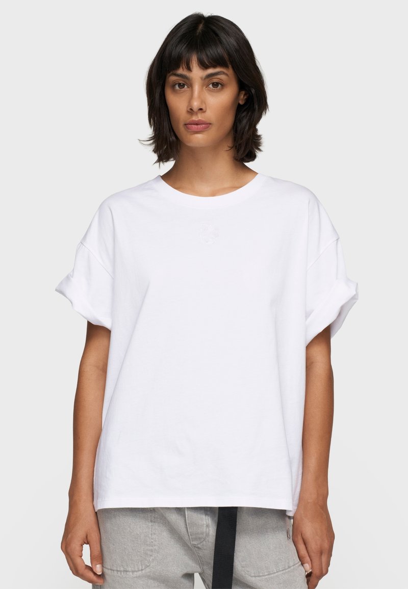 Camiseta blanca de gran tamaño con mangas cortas y enrolladas, y un escote redondo. Presenta un sutil bordado en el pecho. Tela de algodón suave.