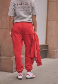 Red sweatpants with elastic cuffs, featuring a back pocket, paired with a gray short-sleeve shirt. White sneakers with red accents.